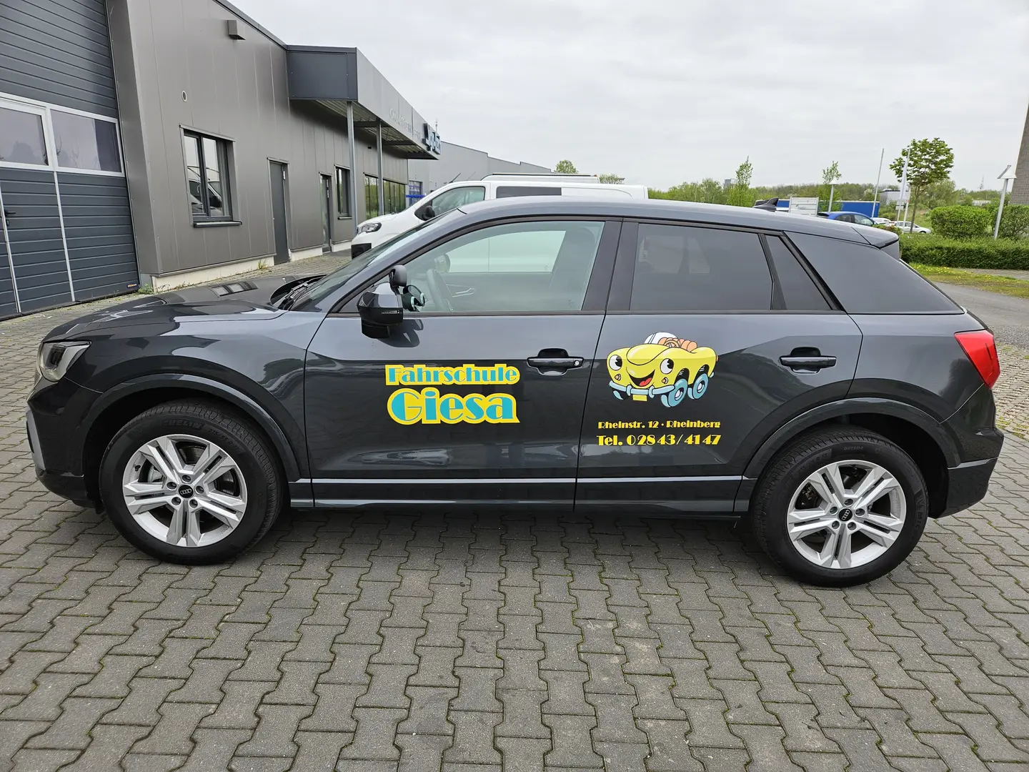 Audi Q2, mit Werbung Fahrschule Giesa (Logo & Schrift), vor der Werkstatt, die das Fahrzeug beklebt hat