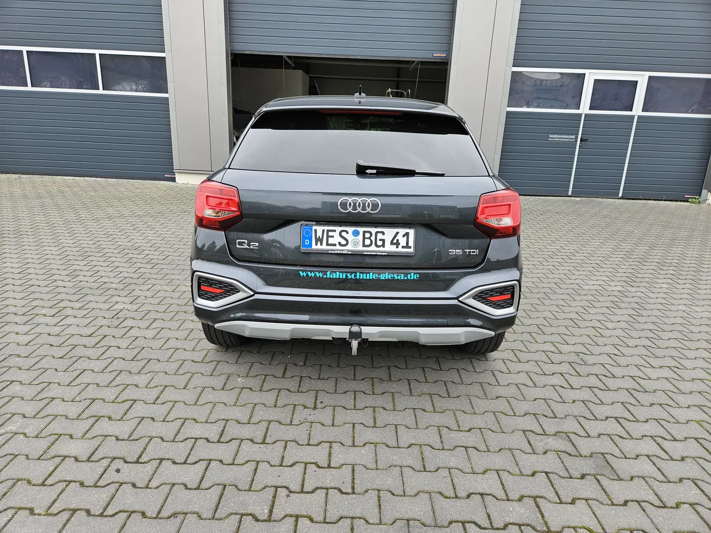 Audi Q2, mit Werbung Fahrschule Giesa (Logo & Schrift), vor der Werkstatt, die das Fahrzeug beklebt hat