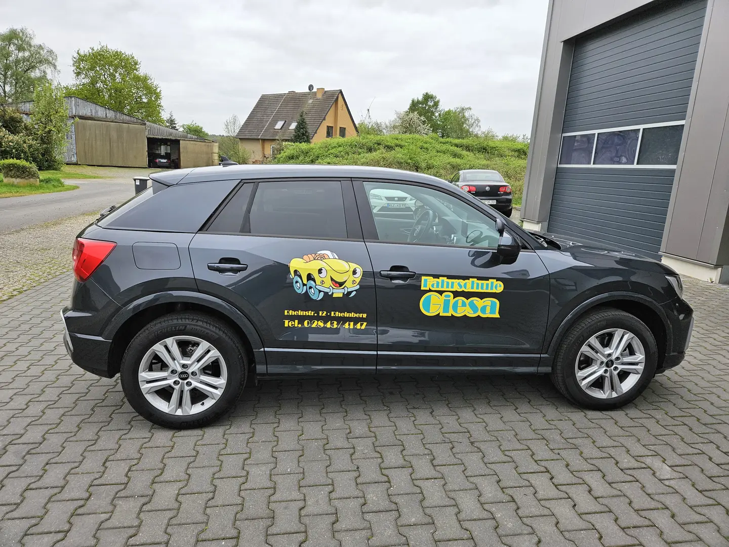 Audi Q2, mit Werbung Fahrschule Giesa (Logo & Schrift), vor der Werkstatt, die das Fahrzeug beklebt hat